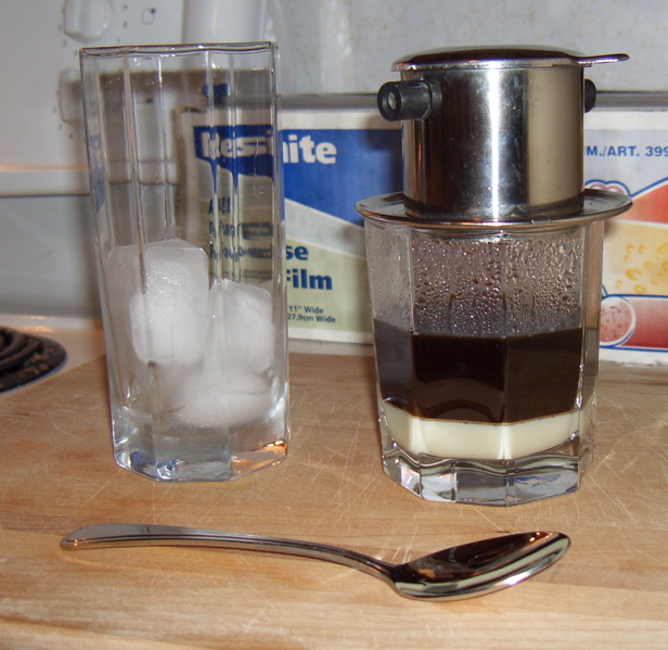 Vietnamese coffee dripping through a phin filter beside a glass of ice