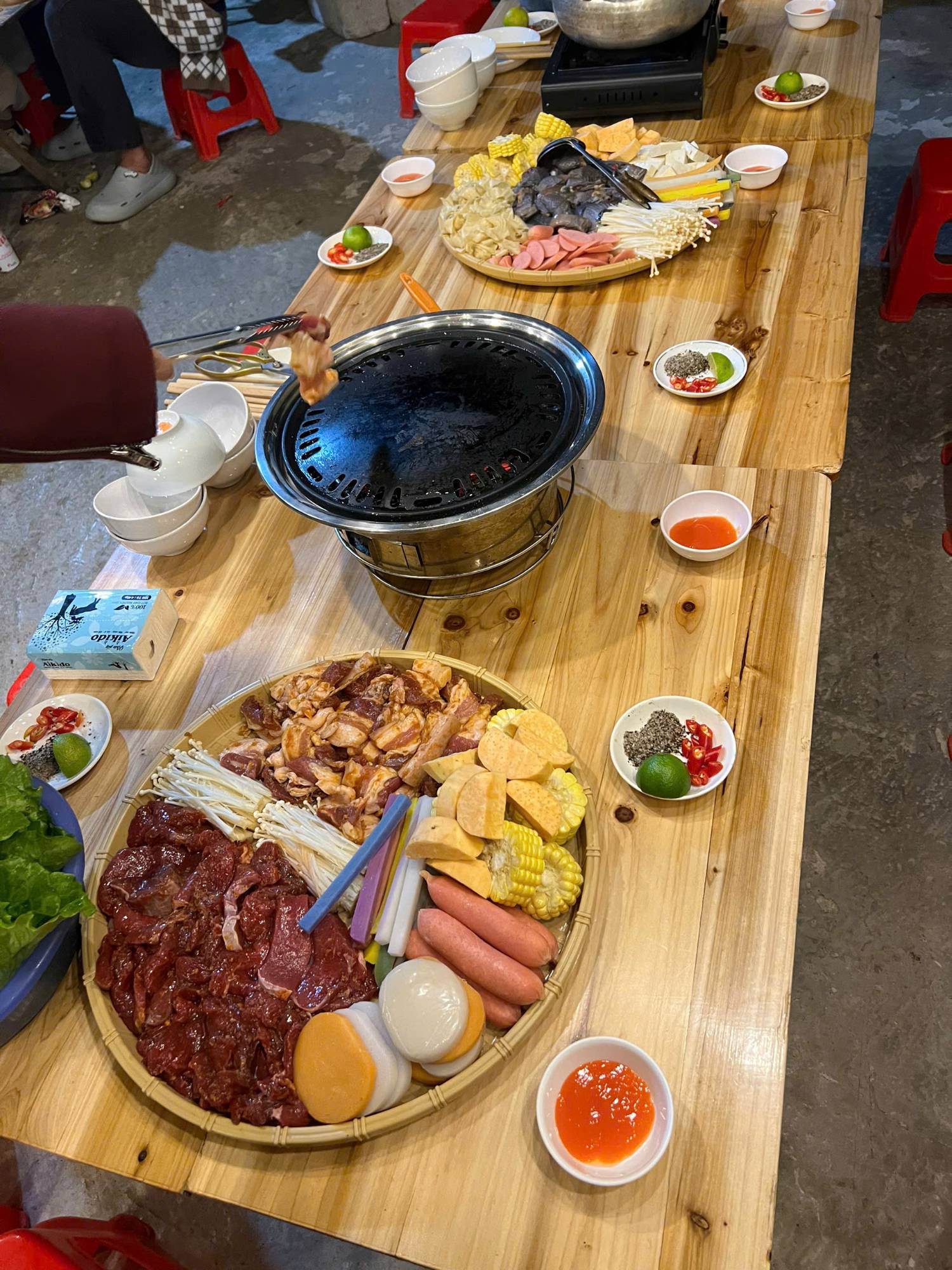Table-top barbecue with trays of marinated meat, corn and mushrooms