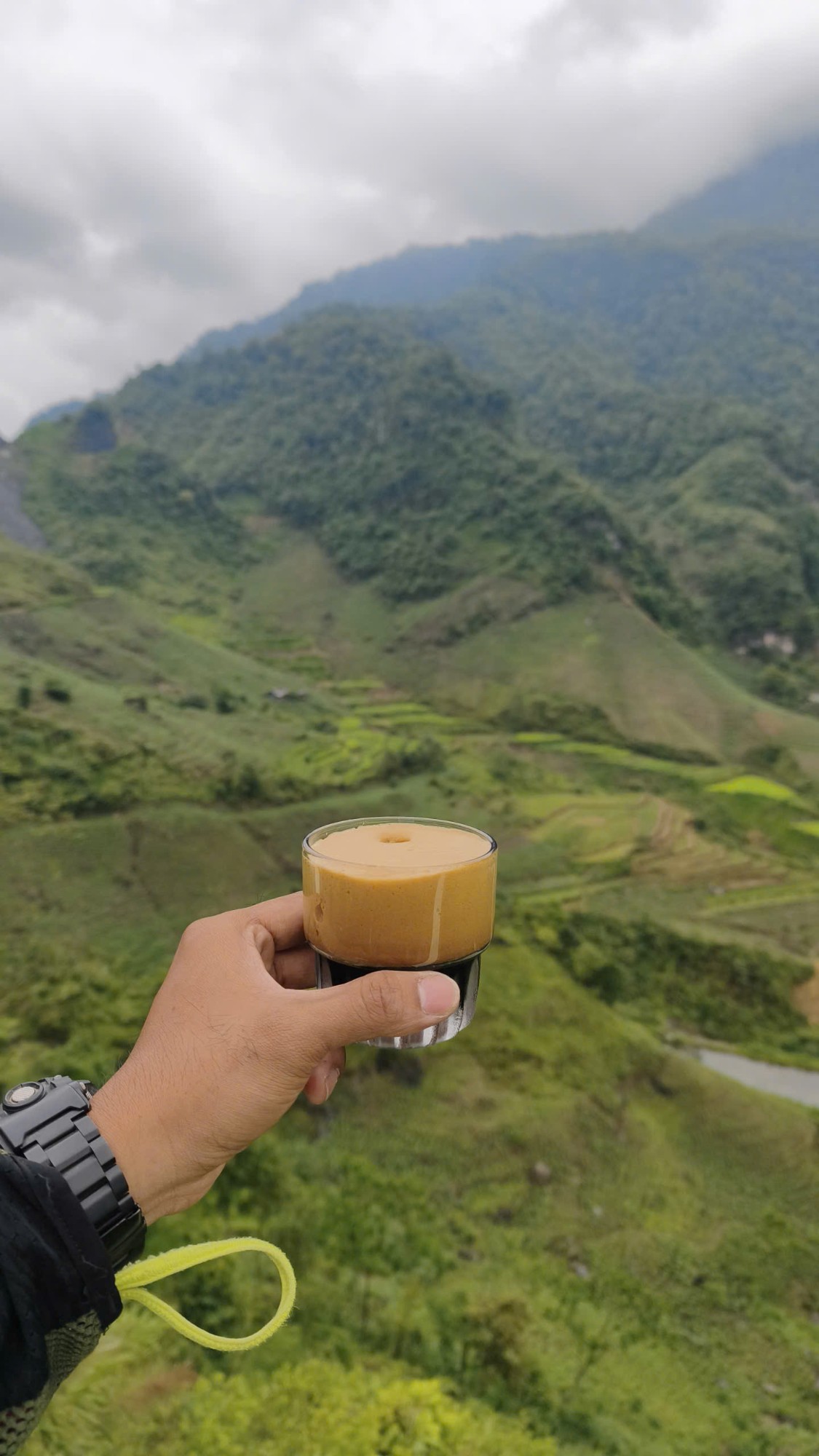 Glass of Vietnamese egg coffee held up over a green valley
