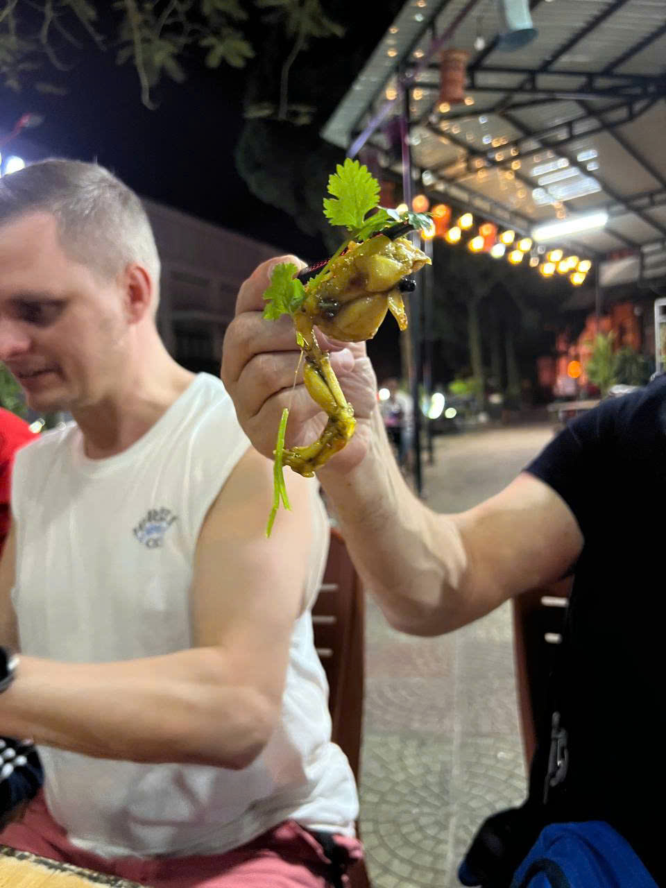 Rider holding up a fried frog at a night food stall