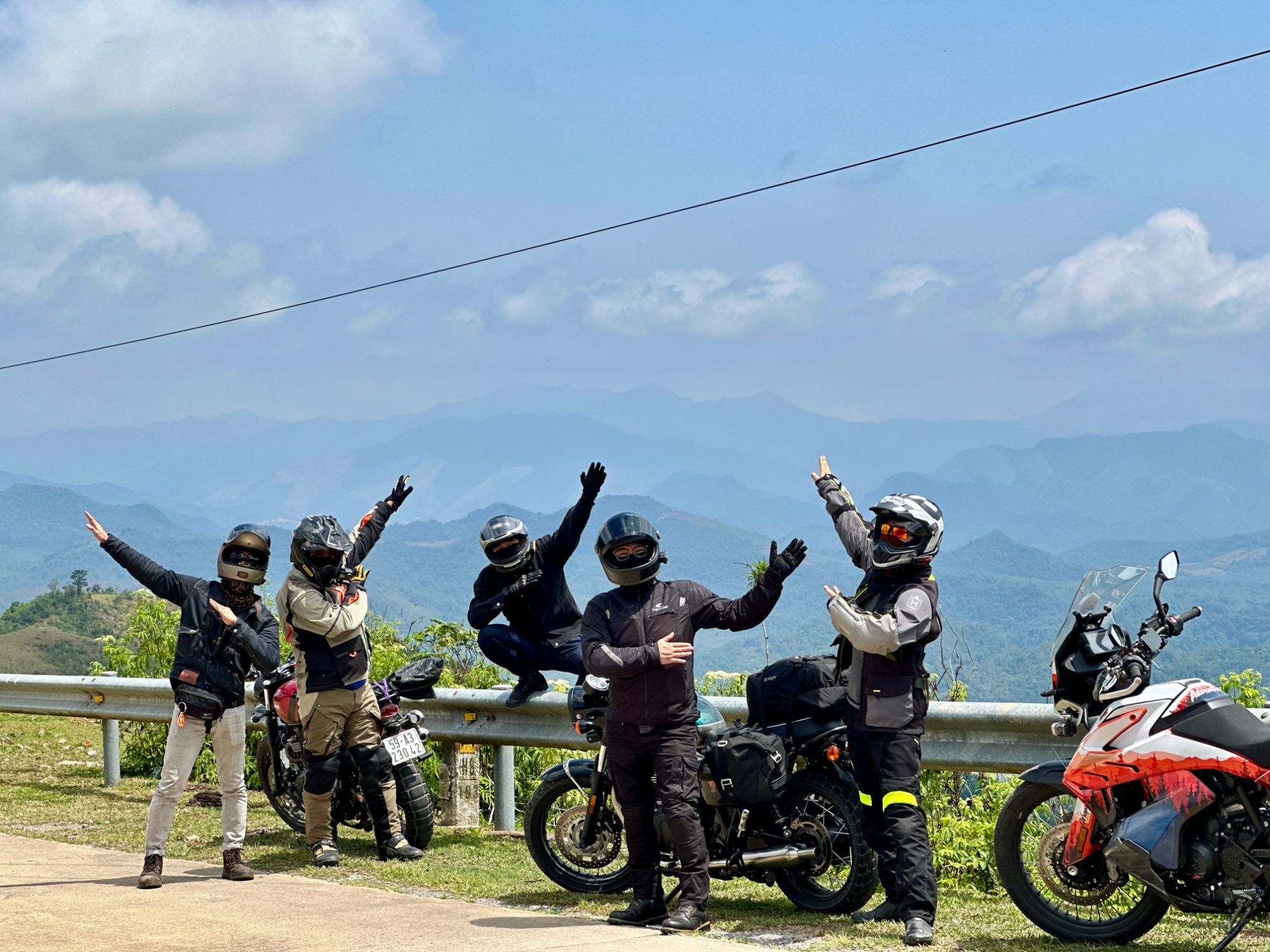 Riders in helmets posing by their bikes above a mountain range