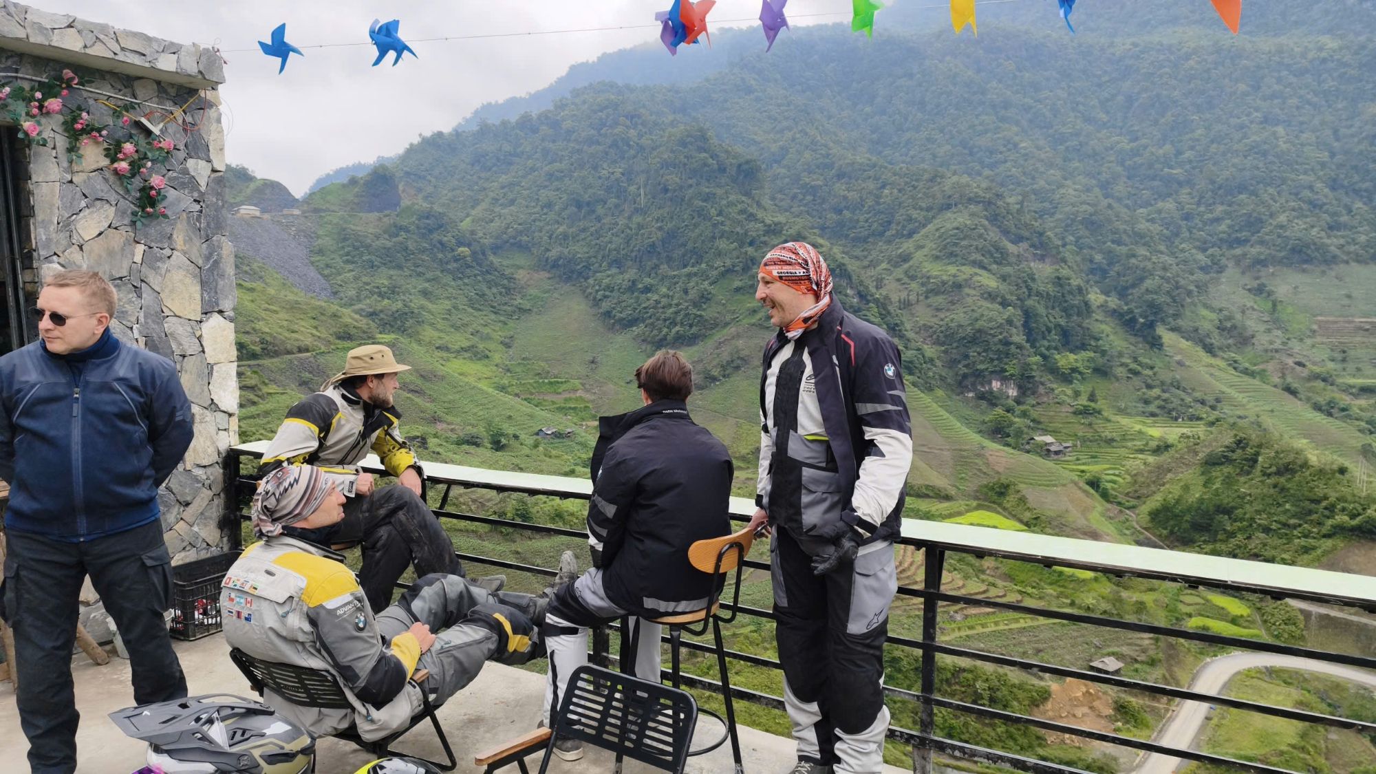 Riders resting on a cafe terrace above green mountains