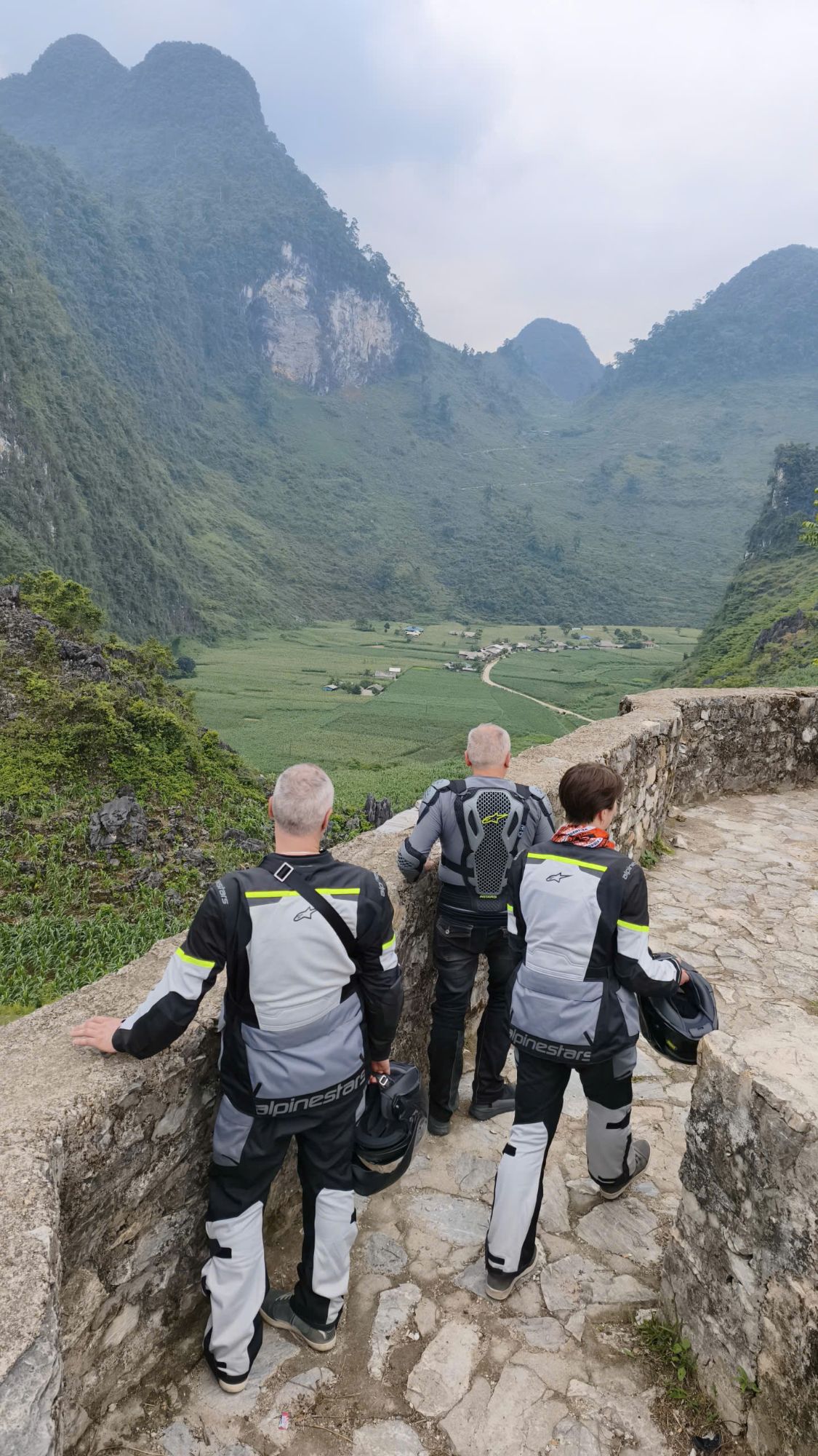 Three riders at a stone lookout above a valley village