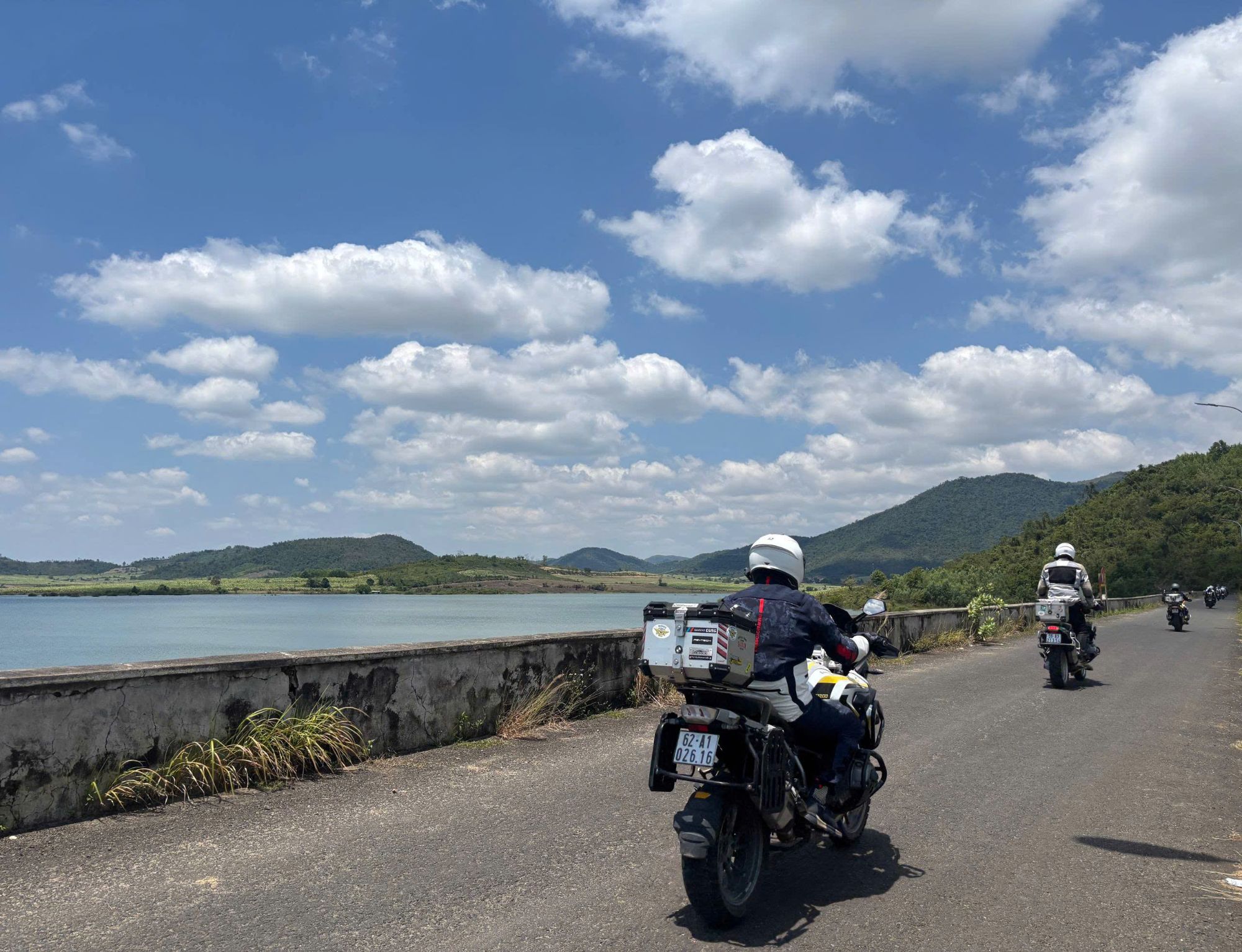 Convoy of bikes riding along a lakeside dam road