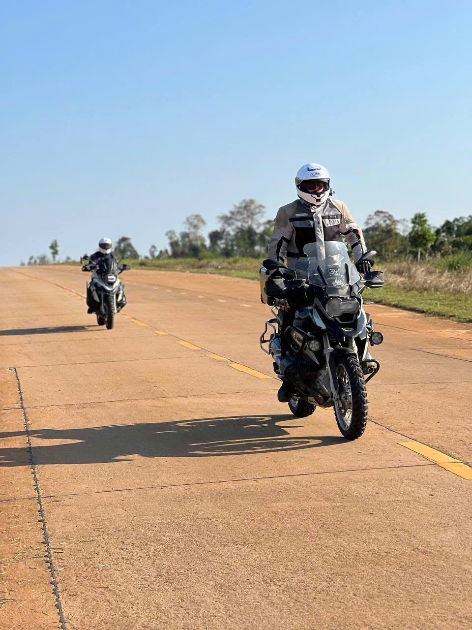 Two BMW GS riders on a wide red-dust highland road