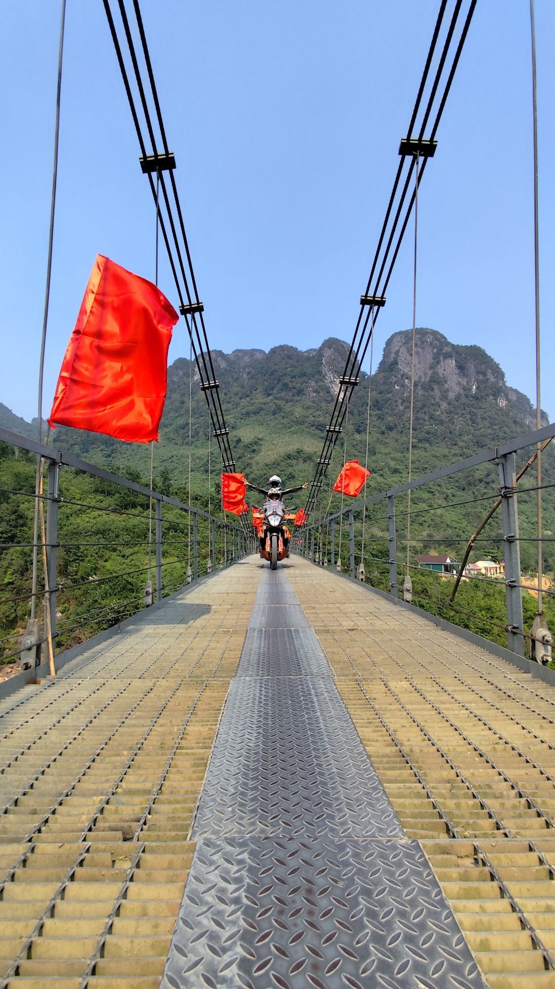 Rider crossing a suspension bridge lined with red flags