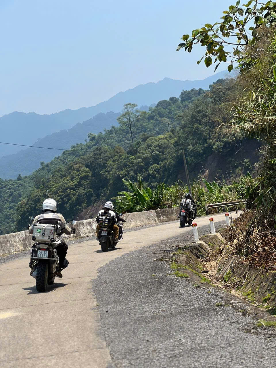 Three riders on a mountain road above a forested valley