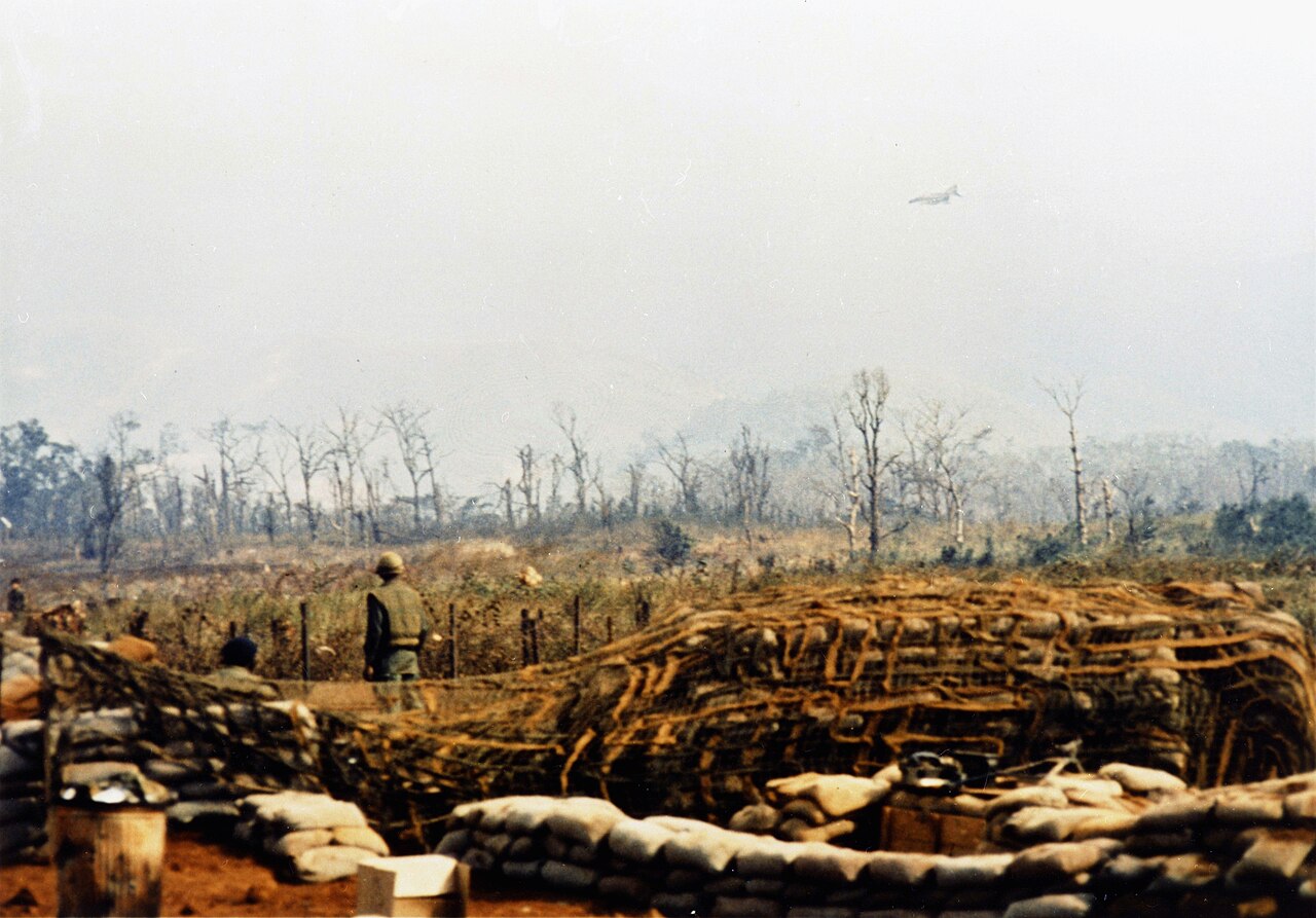 Marines in trenches watching an F-4 Phantom fighter strike the hills beyond the base