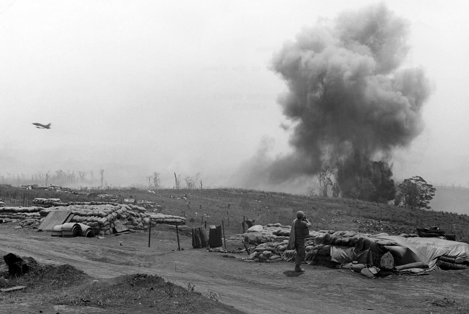 A Marine among sandbagged bunkers at Khe Sanh watches smoke rise from a bomb dropped by a US F-100 jet, March 1968