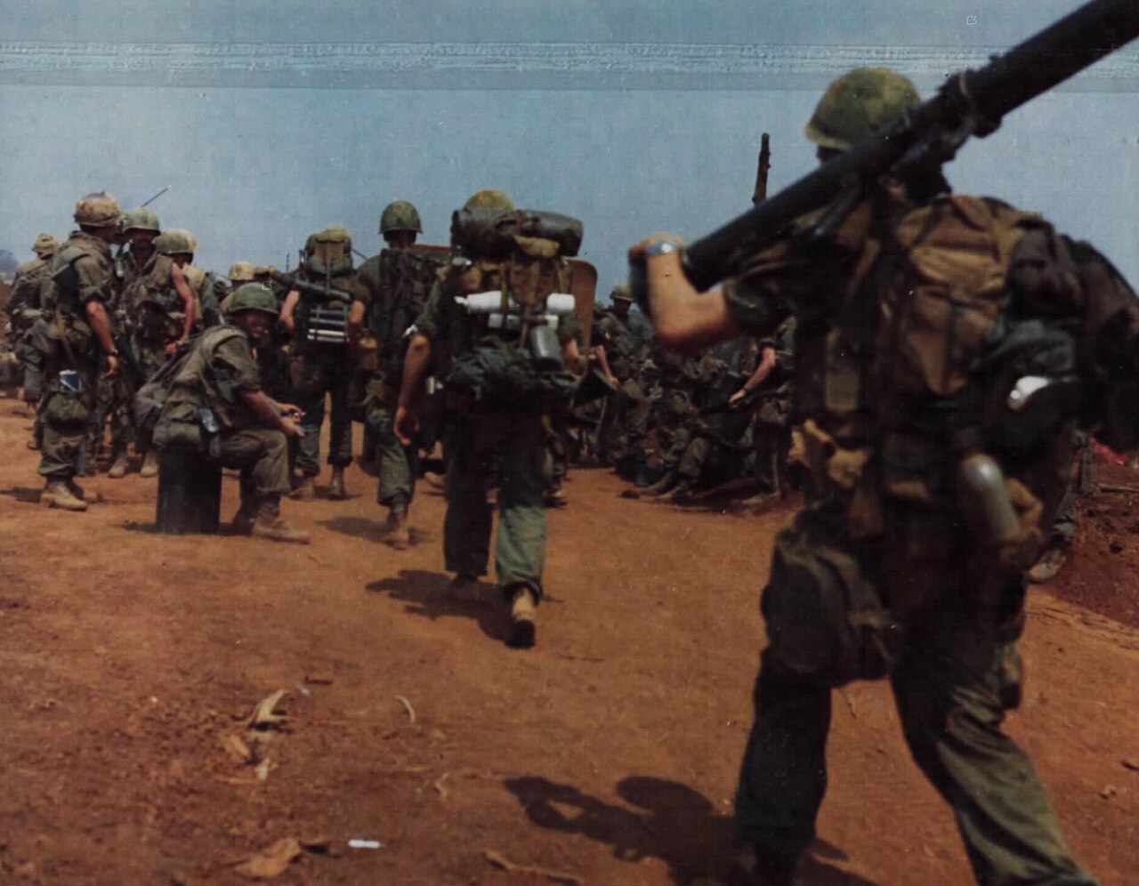 A US Army cavalryman with a machine gun belt watches Marines walking out of the base