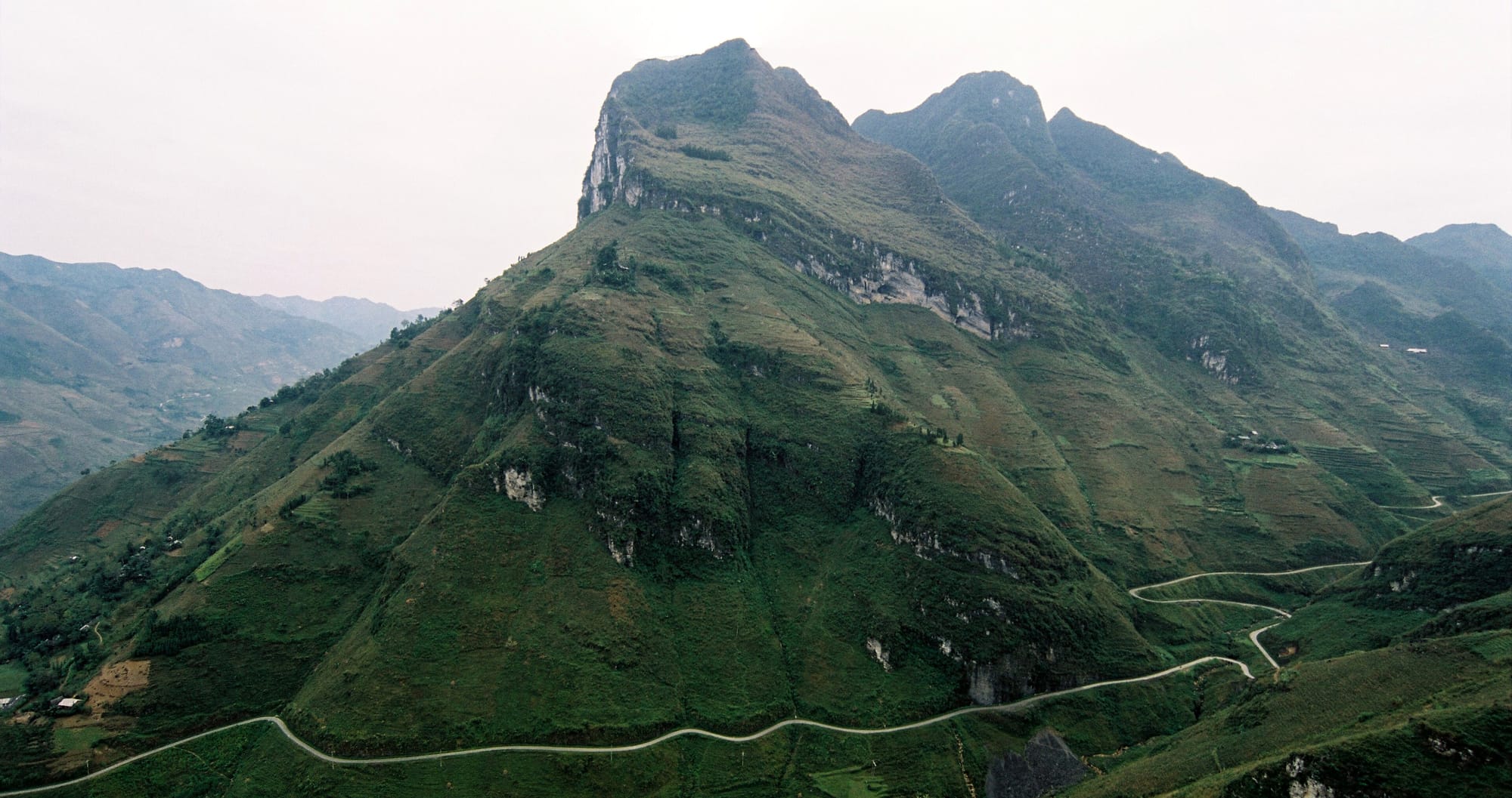 The road over Ma Pi Leng Pass winding along the foot of a steep green karst mountain