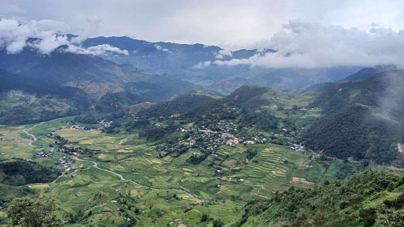 A wide valley of rice terraces and villages below clouds, seen from the mountains at Khau Pha