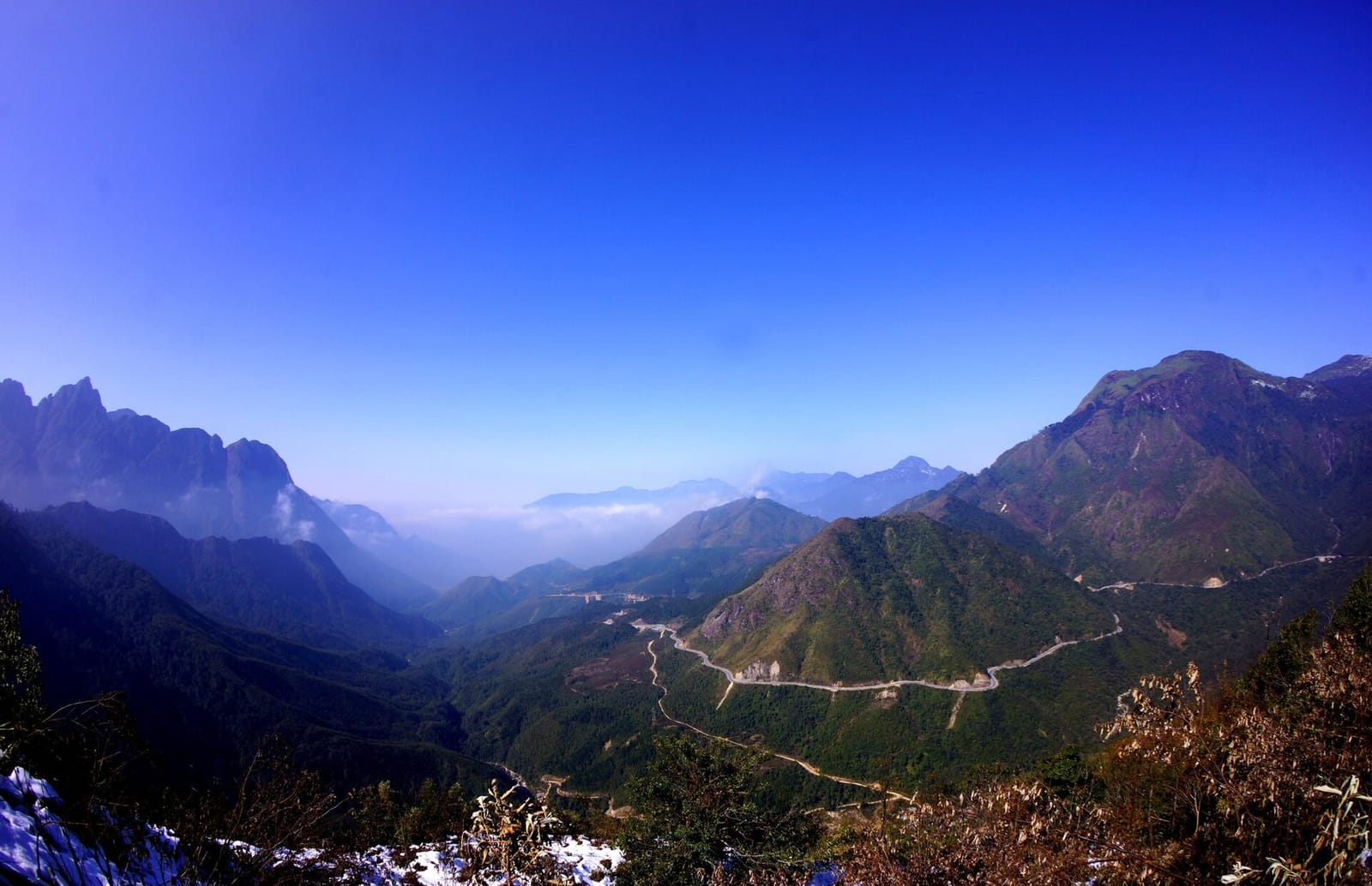 The O Quy Ho road winding along a green valley below high mountains, with snow in the foreground