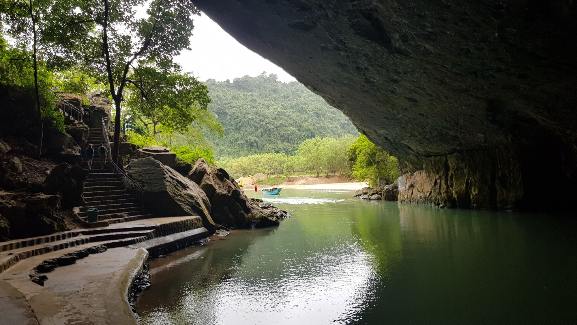 The Son river flowing out of the mouth of Phong Nha Cave, with a tour boat and forested limestone hills beyond