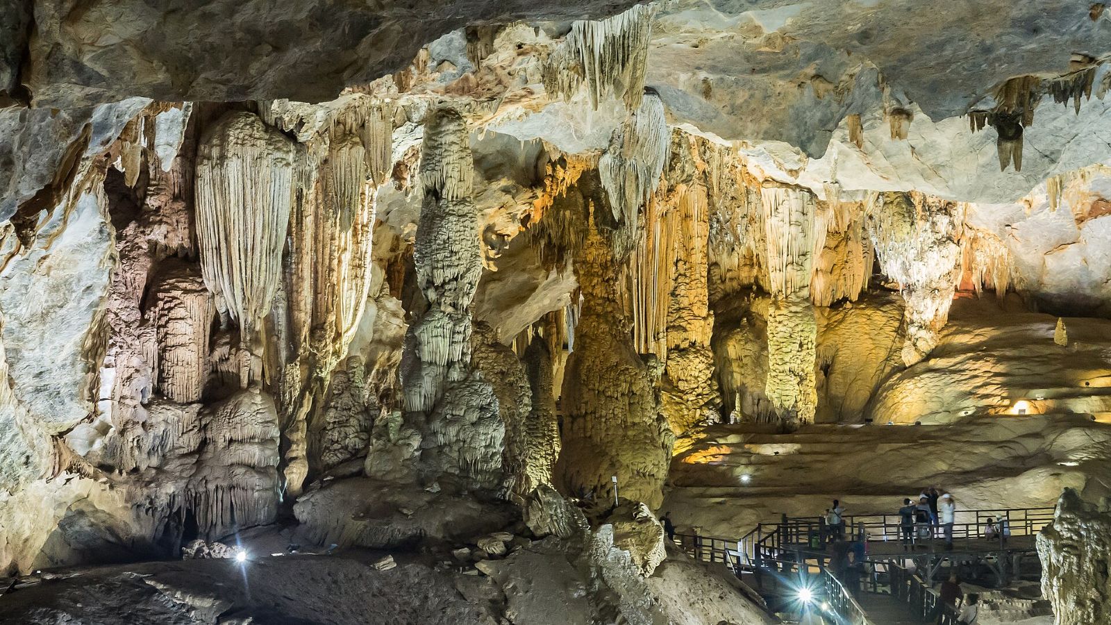 Stalactites and stalagmites lit up inside Paradise Cave, with visitors on the wooden walkway