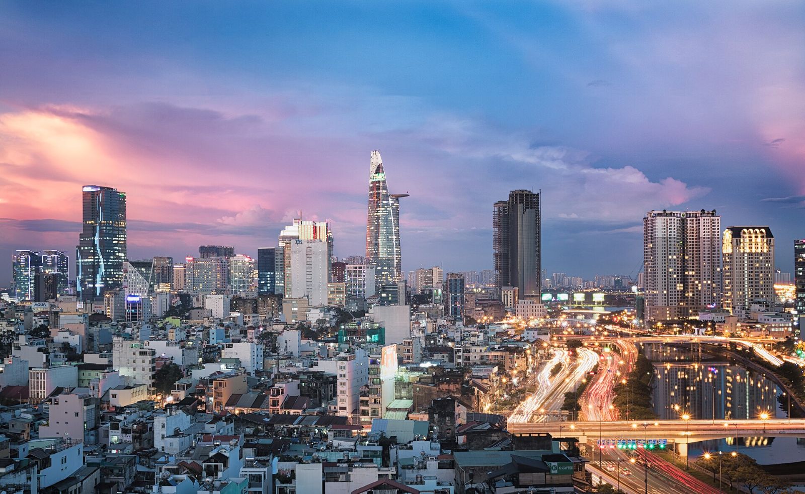 Ho Chi Minh City skyline at sunset, with the Bitexco tower and traffic light trails along the canal