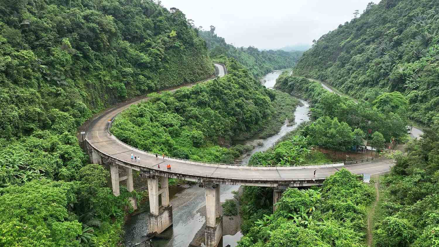 A curved concrete bridge carries the road over a river through thick Truong Son jungle